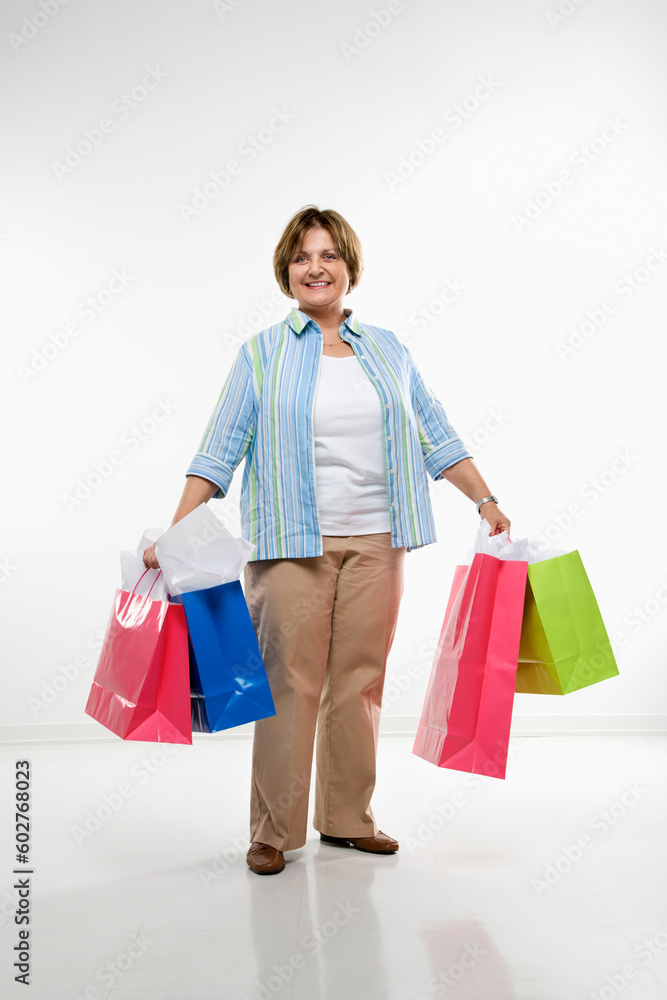 Caucasian middle aged woman holding gift bags smiling at viewer.