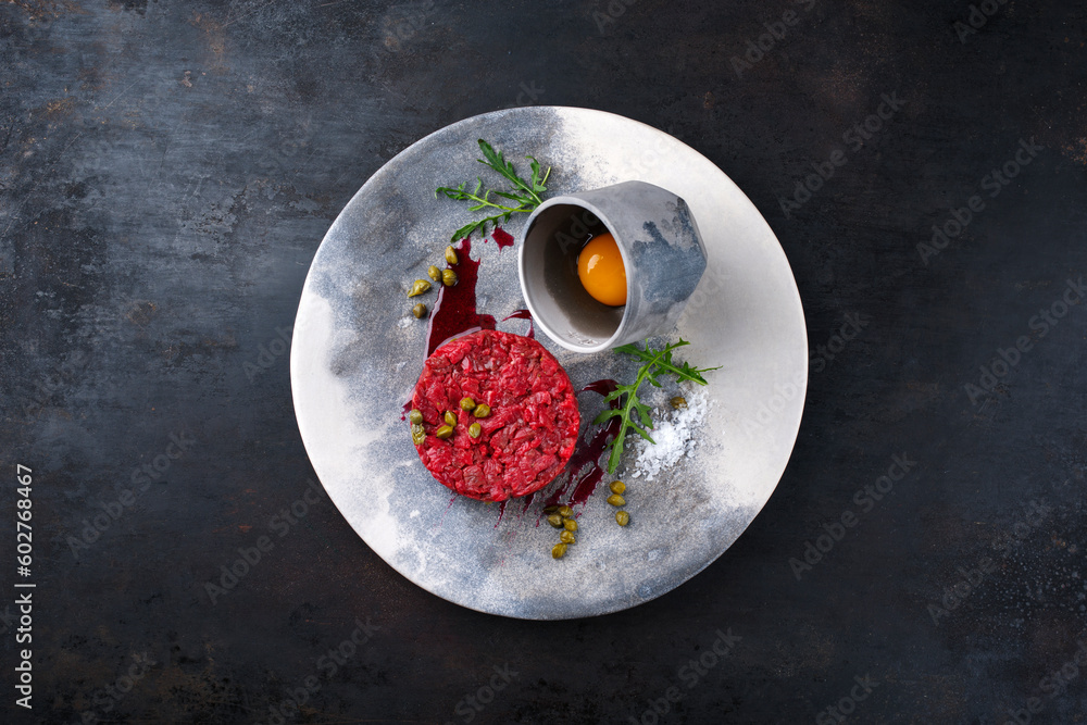 Gourmet Tartar roh aus Rinderfilet mit Ei, Rucola und Kapern serviert als Draufsicht auf einem Design Teller mit Textfreiraum Gourmet Tartar roh aus Rinderfilet mit Ei, Rucola und Kapern serviert als Draufsicht auf einem Design Teller mit Textfreiraum