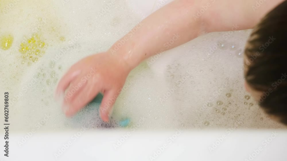 A child is playing in the water with a mechanical wind-up toy of a blue turtle. Baby is playing with toys in the water sitting in a white bath, close-up. Kid about two years old (one year ten months). A child is playing in the water with a mechanical wind-up toy of a blue turtle. Baby is playing with toys in the water sitting in a white bath, close-up. Kid about two years old (one year ten months).