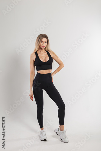 Beautiful athletic fitness woman model with blond hair in trendy sportswear with leggings, top and sneakers on a white background in the studio