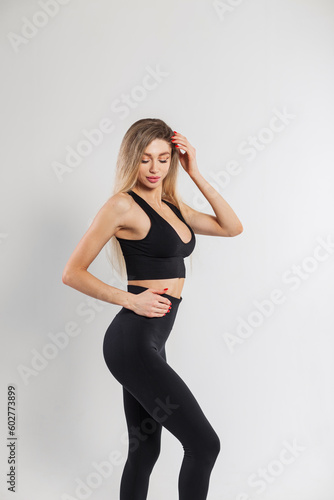 Beautiful young woman fit model with a slender body in fashionable black sportswear with a top and leggings posing on a white background © alones