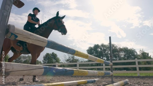Chestnut horse, ridden by a female rider in a black equestrian outfit, jumping over hurdles in the open arena, low angle shot.