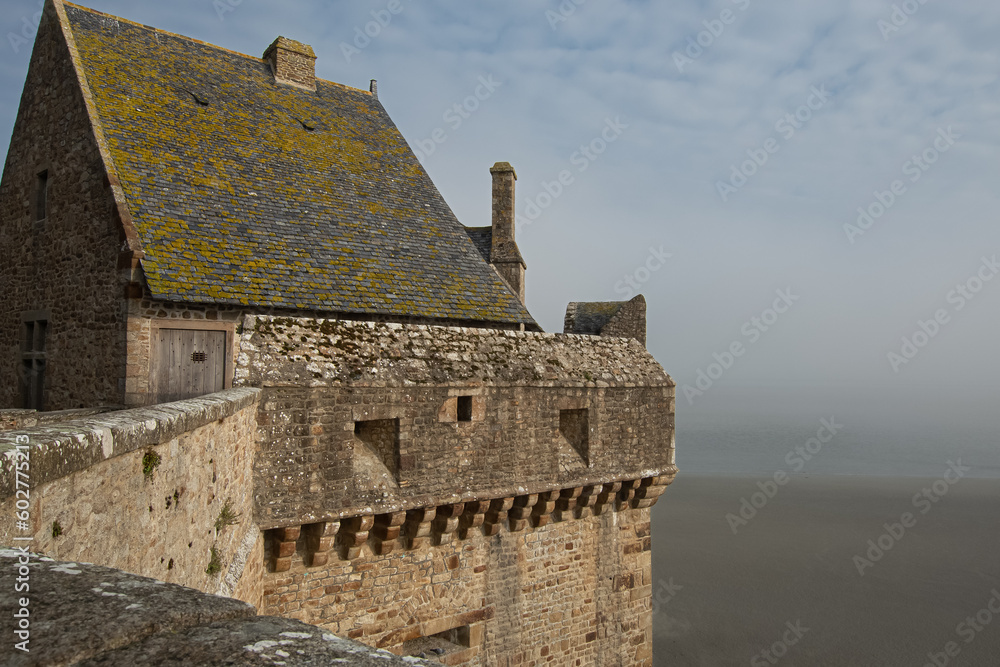 The Abbey at Mont Saint Michel shrouded in light fog, towers over the village below