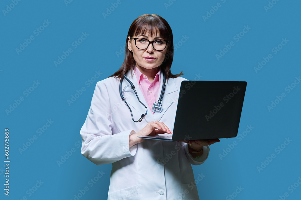 Mature female doctor using laptop on blue background Mature female doctor using laptop on blue background