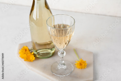 Board with bottle and glass of dandelion wine on white table