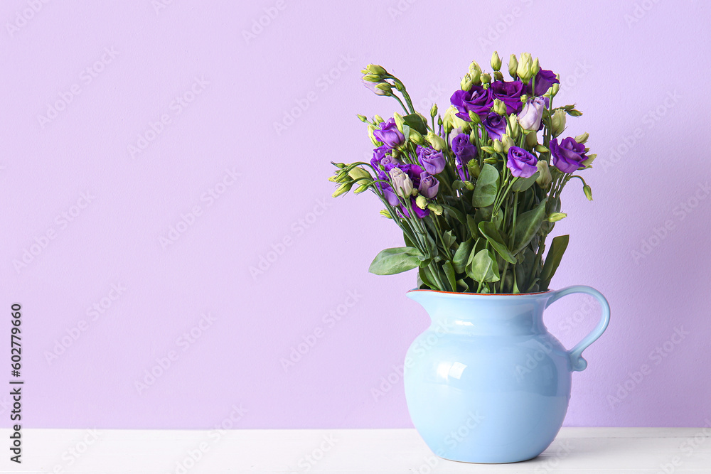 Jug with eustoma flowers on table near lilac wall