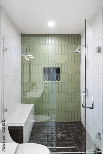 Green hexagon style tiled shower with a black hexagon tile built in shelf, with white square tiles on to the sides and a glass door