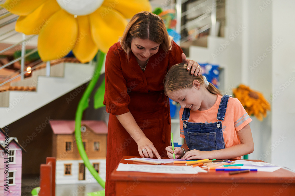 Creative kids during an art class in a daycare center or elementary school classroom drawing with female teacher. Creative kids during an art class in a daycare center or elementary school classroom drawing with female teacher.