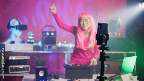 Asian artist mixing techno sound recording music session with smartphone camera, enjoying performing at electronic party in night club. Musician playing remix using professional audio equipment