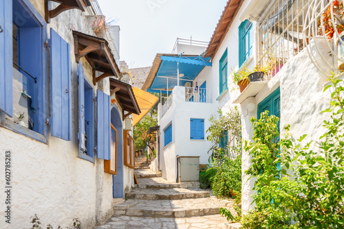 Narrow street in old european town in summer sunny day. Beautiful scenic old ancient white houses  cafe and shops with green plants. Popular tourist vacation destination  mediterranean architecture