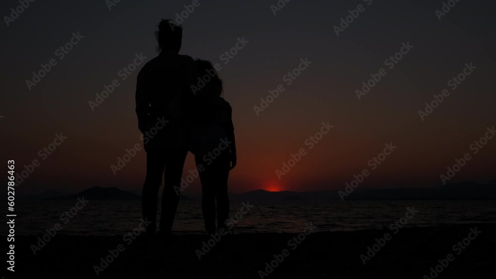Silhouette of a mother hugging a child at sunset. Rear view of a woman with her daughter enjoying the sea sunset at sunset. Silhouette of a mother hugging a child at sunset. Rear view of a woman with her daughter enjoying the sea sunset at sunset.