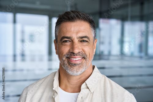 Headshot close up portrait of indian or latin confident mature good looking middle age leader, ceo male businessman on blur office background. Handsome hispanic senior business man smiling at camera.