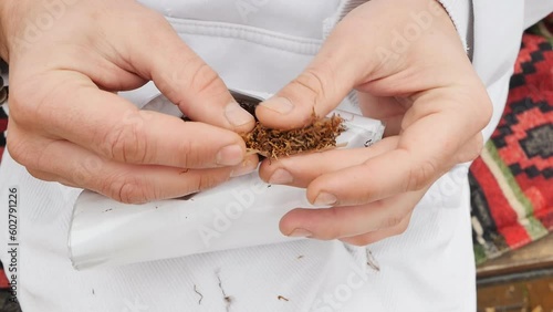 Close-up of a man's hand holding tissue paper and tobacco with his fingers forms a cigarette with marijuana. A young guy made a homemade cigarette photo