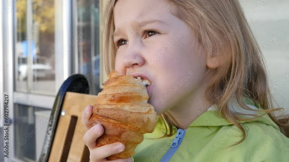 A cute european girl takes a bite and eats a croissant sitting on a bench outdoors. Snack on delicious pastries with cream filling A cute european girl takes a bite and eats a croissant sitting on a bench outdoors. Snack on delicious pastries with cream filling