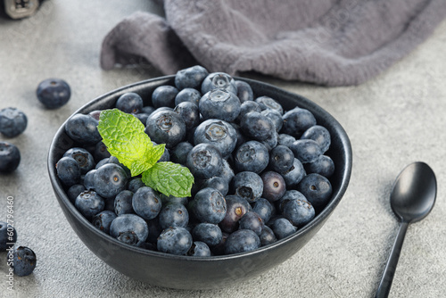 Natural blueberries in a black bowl with mint on gray background, close up