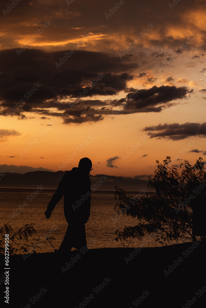 Obraz premium Man walking at sunset at bay.