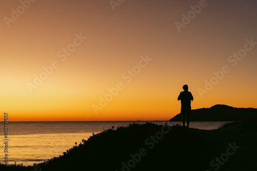 Silhouette of man standing on sand dune overlooking Jimmy s Beach at sunrise. Hawks Nest  NSW Australia