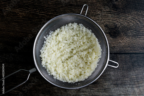 Thawed Frozen Cauliflower Rice in a Mesh Strainer: Rice cauliflower in a colander placed over a mixing bowl