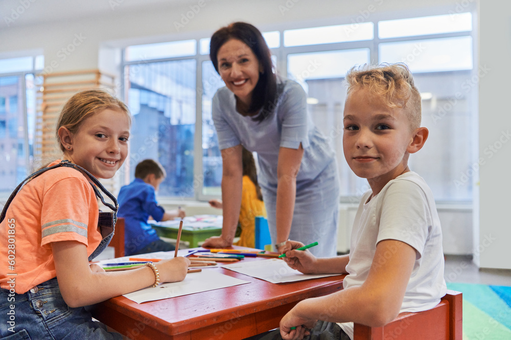 Creative kids during an art class in a daycare center or elementary school classroom drawing with female teacher. Creative kids during an art class in a daycare center or elementary school classroom drawing with female teacher.