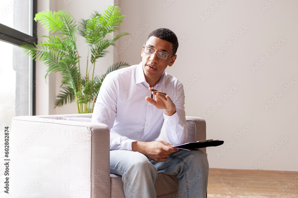 male african american psychologist in armchair consults and tells, session with psychotherapist, psychologist calms down - obrazy, fototapety, plakaty 