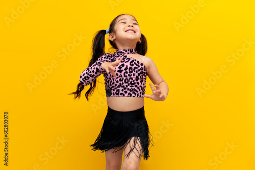 little asian girl in dance outfit dances chachacha on yellow isolated background, korean child dancer trains dance photo