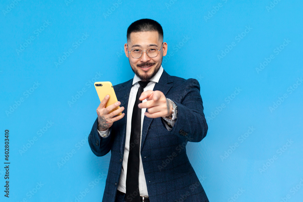 hey you. successful asian businessman in suit and glasses uses smartphone and points chooses you hey you. successful asian businessman in suit and glasses uses smartphone and points chooses you