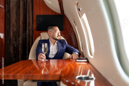 Принти на полотні asian businessman in suit and glasses with glass of champagne flies in private l