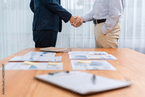 Foto Two businesspeople shake hand after signing contract document to merge their partnerships in conference room and finalized pile of papers of financial report and data analysis on meeting table