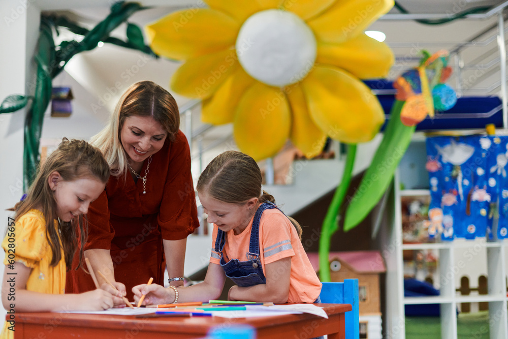 Creative kids during an art class in a daycare center or elementary school classroom drawing with female teacher. Creative kids during an art class in a daycare center or elementary school classroom drawing with female teacher.