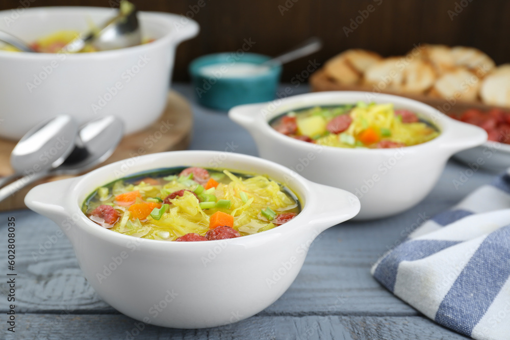 Delicious sauerkraut soup with smoked sausages and green onion on grey wooden table Delicious sauerkraut soup with smoked sausages and green onion on grey wooden table
