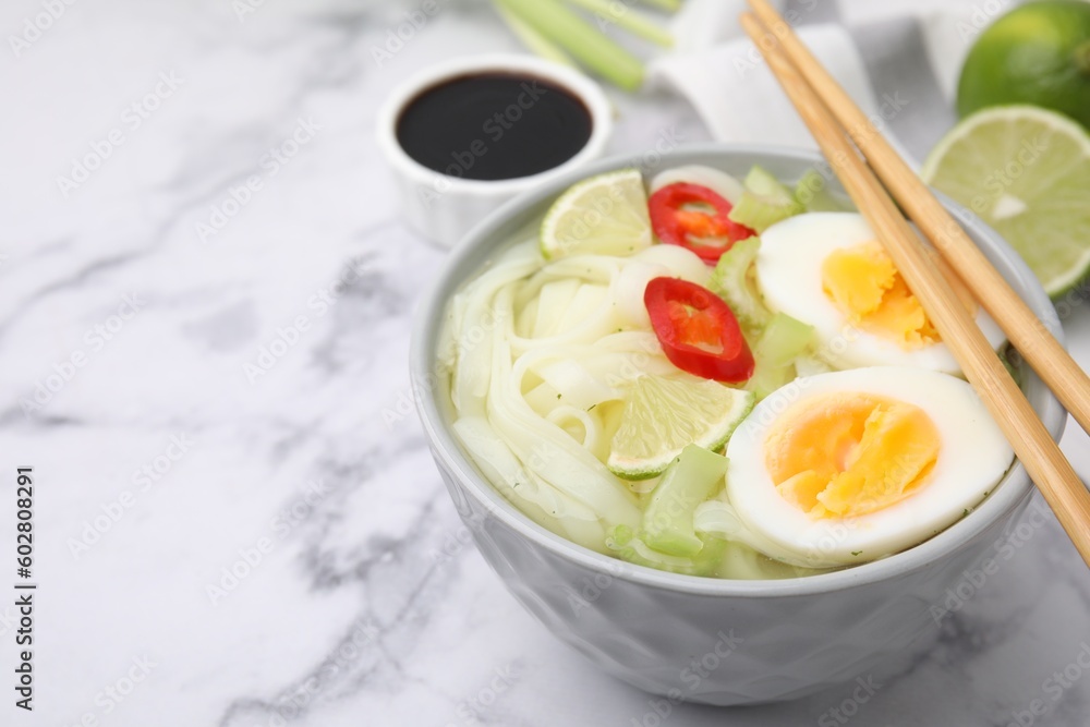 Bowl of delicious rice noodle soup with celery and egg on white marble table, closeup. Space for text Bowl of delicious rice noodle soup with celery and egg on white marble table, closeup. Space for text