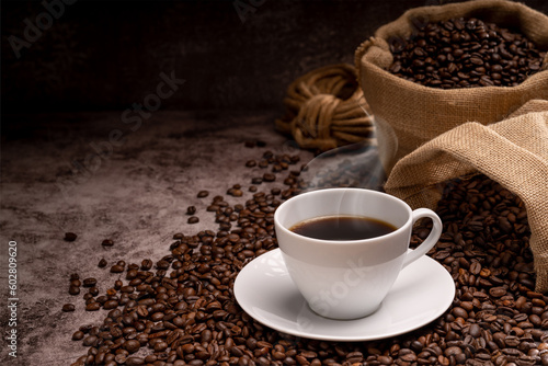 coffeeHot coffee in a white coffee cup and many coffee beans placed around on a wooden table in a warm, light atmosphere, on dark background. photo