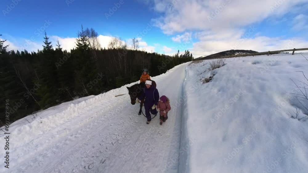 8 year old boy with autism horseback riding during winter with mother and younger sister walking beside 8 year old boy with autism horseback riding during winter with mother and younger sister walking beside