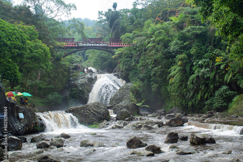 baturraden tropical waterfall in the middle of rain forest and red bridge on the top photo