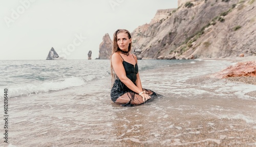 Woman summer travel sea. Happy tourist in black dress enjoy taking picture outdoors for memories. Woman traveler posing on sea beach surrounded by volcanic mountains  sharing travel adventure journey