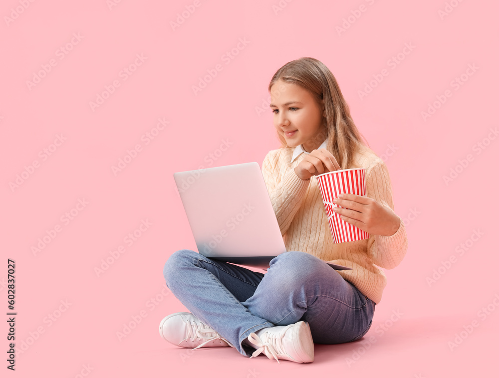 Little girl with popcorn and laptop watching movie on pink background Little girl with popcorn and laptop watching movie on pink background