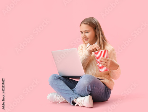 Little girl with popcorn and laptop watching movie on pink background