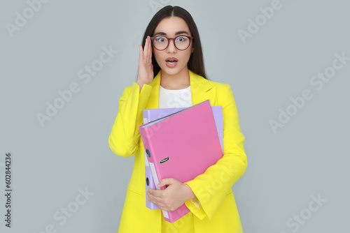 Young female intern with eyeglasses and folders on grey background