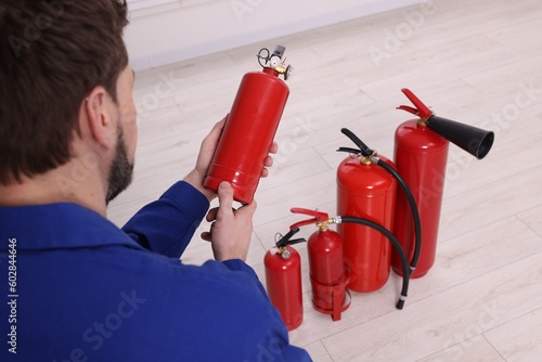 Man checking quality of fire extinguishers indoors, closeup