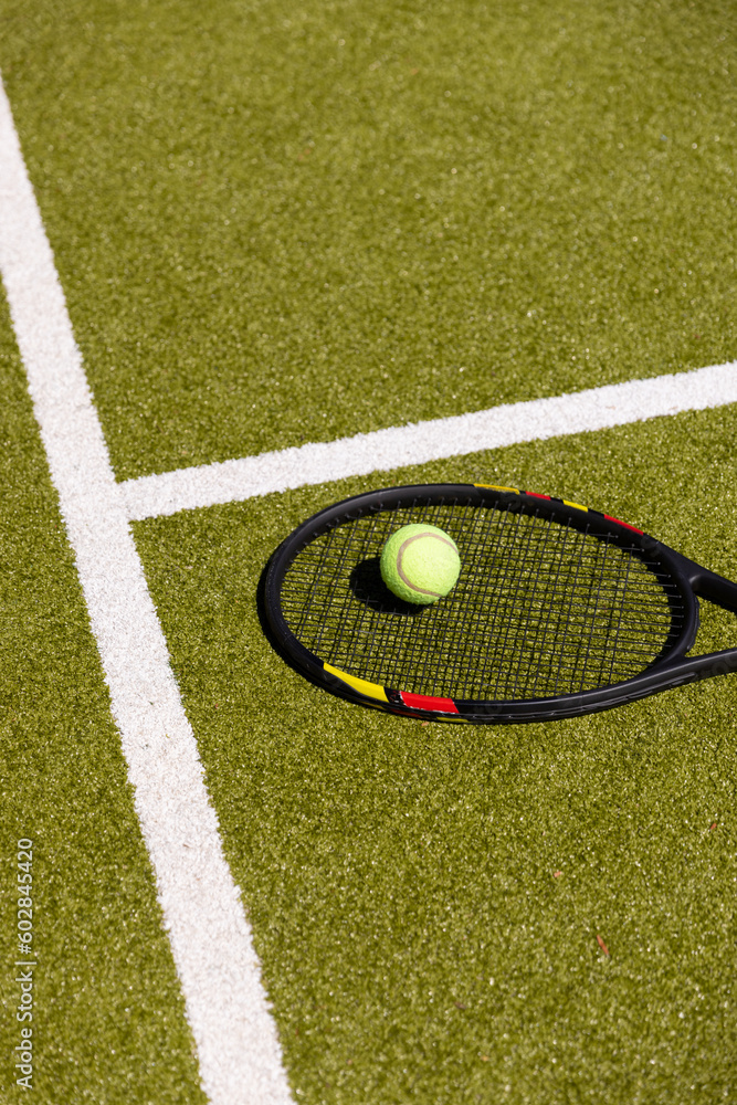 Tennis ball on tennis racket lying on sunny outdoor grass tennis court, with copy space