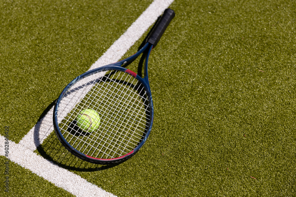 Tennis ball on tennis racket lying on sunny outdoor grass tennis court, with copy space