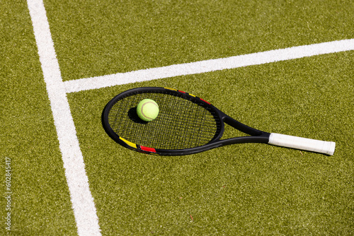 Tennis ball and racket on the ground of sunny outdoor grass tennis court