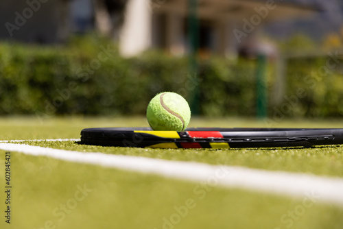 Tennis ball on racket on the ground on sunny outdoor grass tennis court
