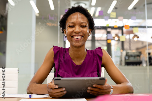 Portrait of smiling african american businesswoman using digital tablet while sitting at desk