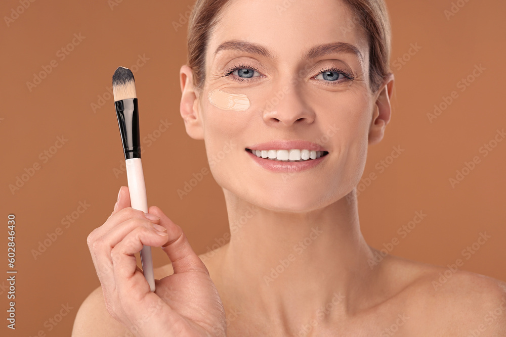 Woman with swatch of foundation and makeup brush against brown background Woman with swatch of foundation and makeup brush against brown background