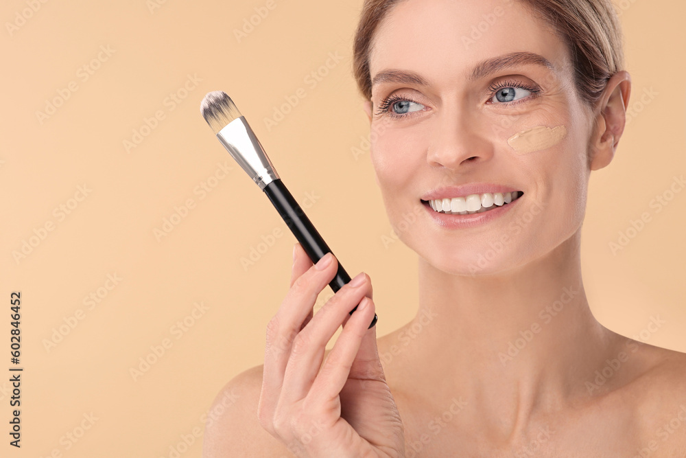 Woman with swatch of foundation holding makeup brush on beige background. Space for text Woman with swatch of foundation holding makeup brush on beige background. Space for text