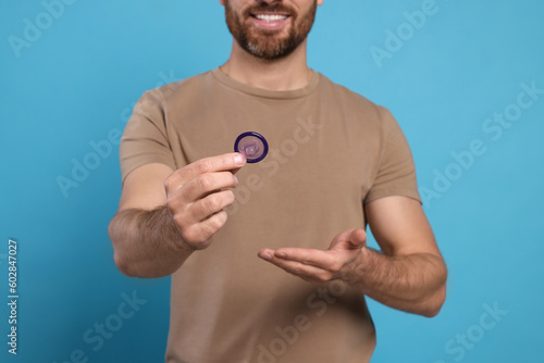 Man holding condom on light blue background, closeup. Safe sex