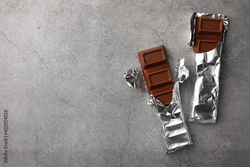 Tasty chocolate bars wrapped in foil on grey table, flat lay. Space for text