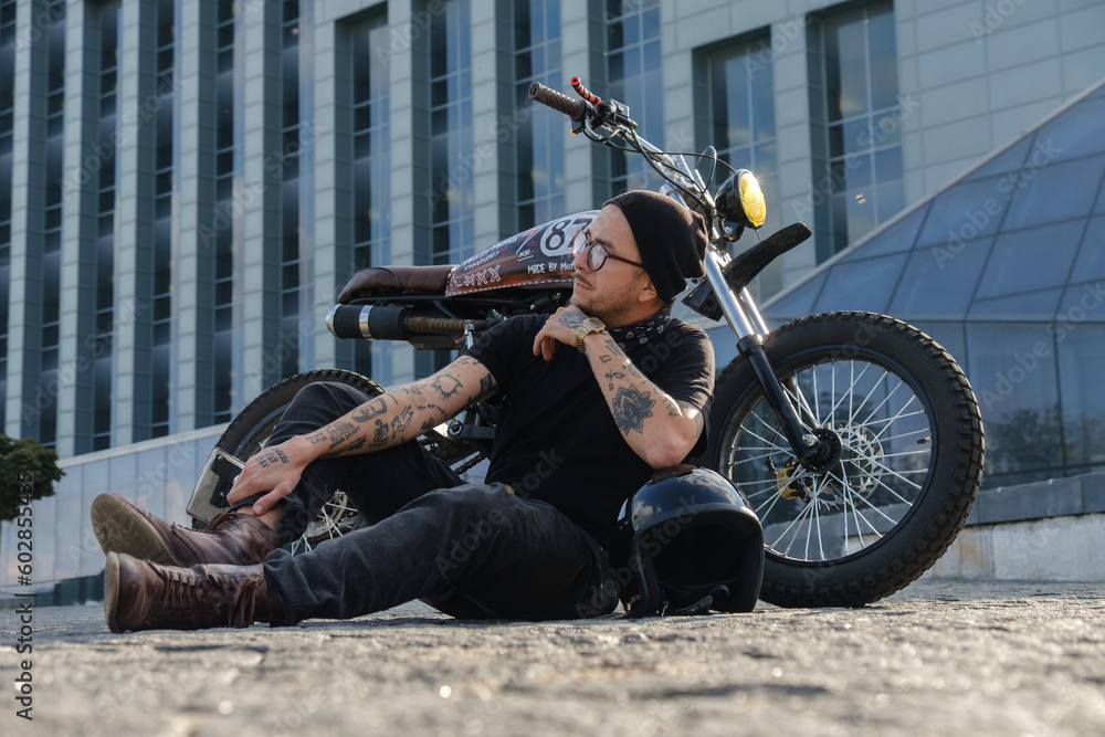 Shot of individual motorcycle driver posing near huge city building.