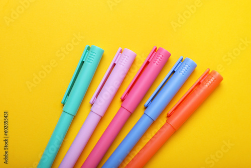 Many colorful markers on yellow background, above view